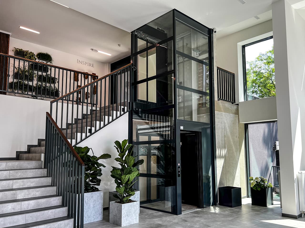 Black Cibes cabin lift with glazed shaft surrounded by green plants.