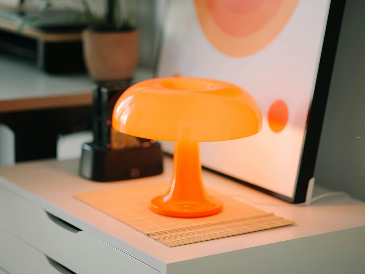 Colourful Nessino table lamp by Artemide in bright orange polycarbonate on a white chest of drawers.