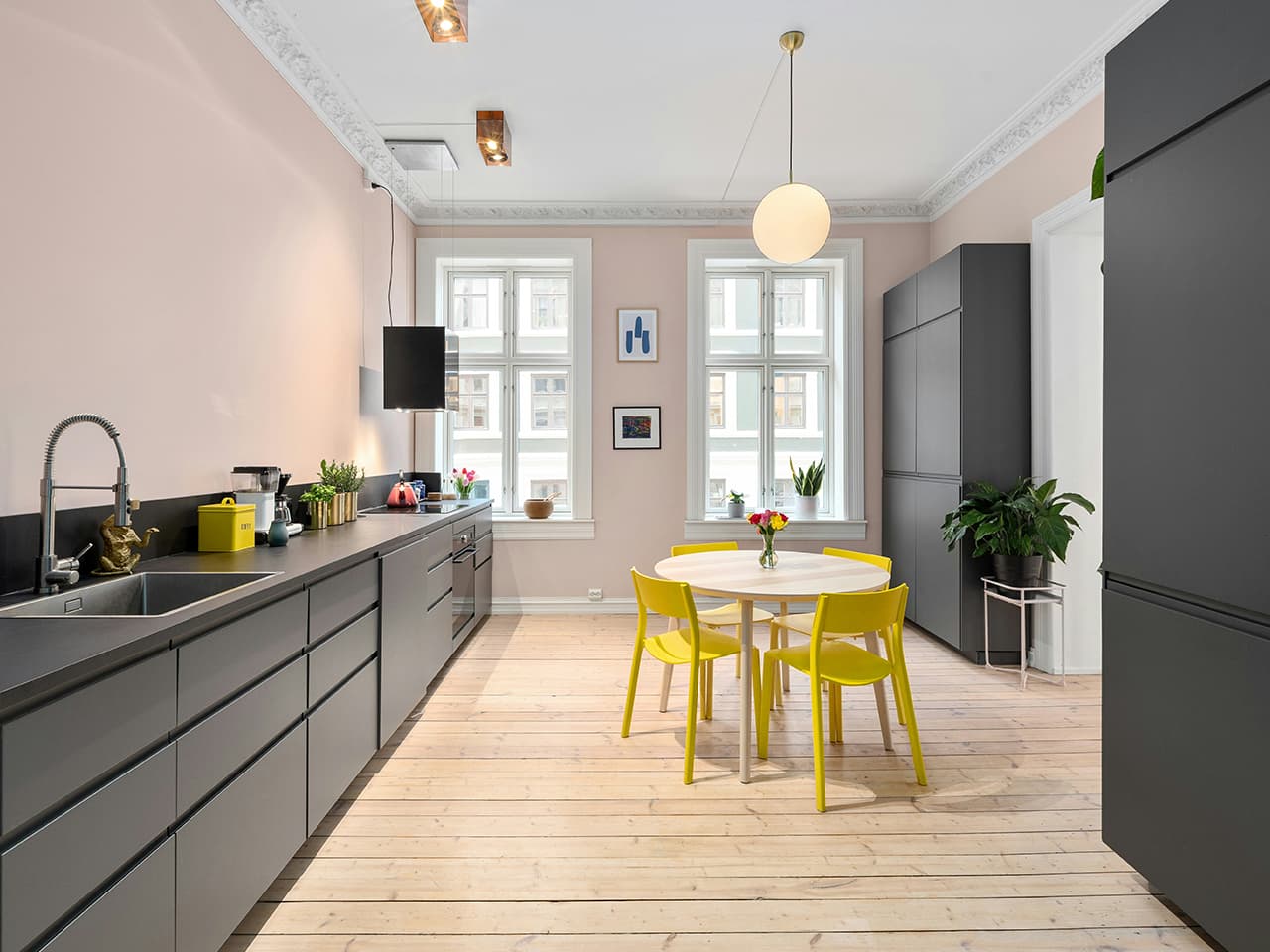 Minimalist kitchen with light pink walls, dark grey cabinets and bright yellow kitechen table and chairs in a turn of the century apartment.