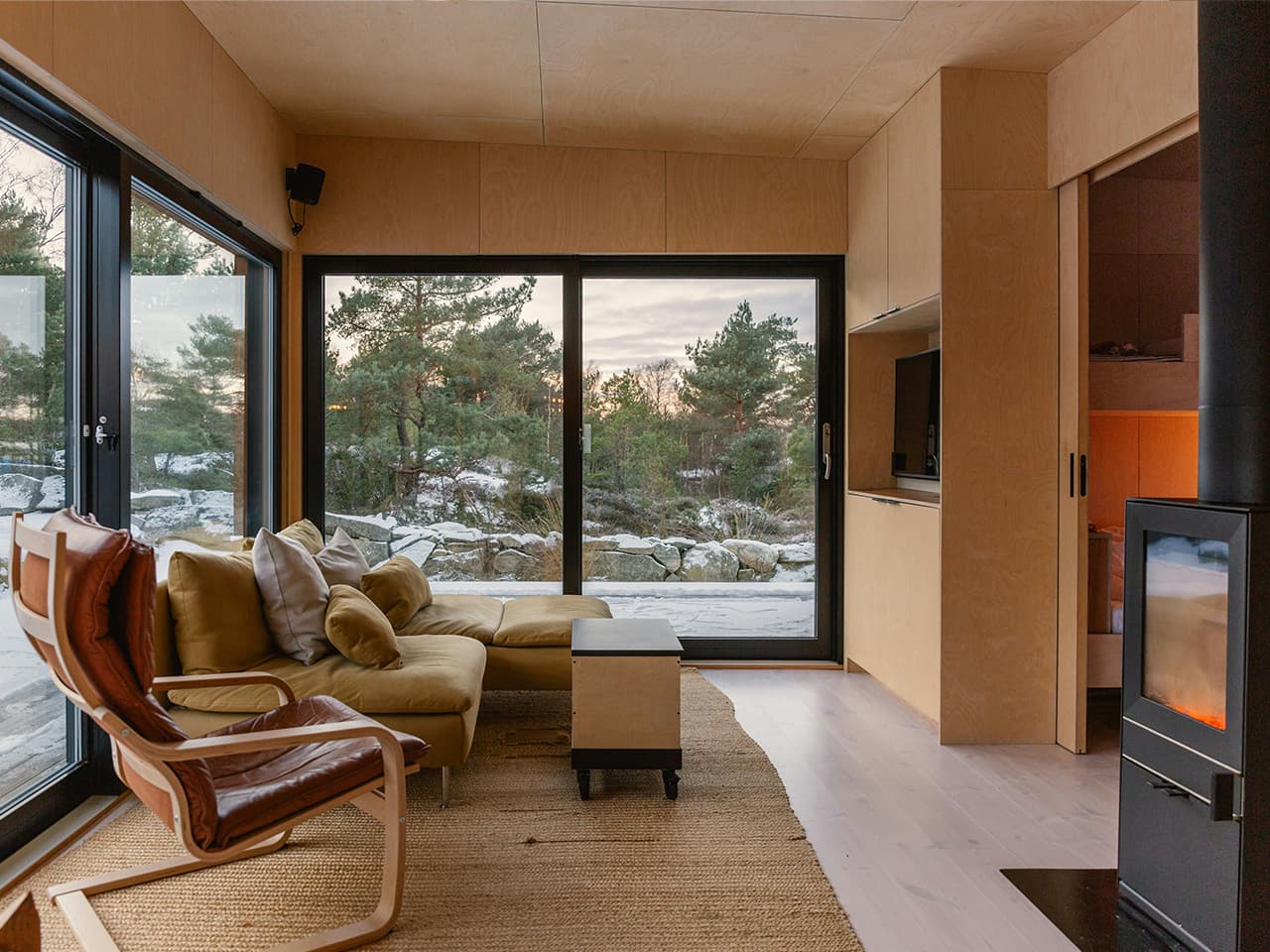 Sleek modern cabin interior with light wood panels, Scandinavian style seating and a wood burner.