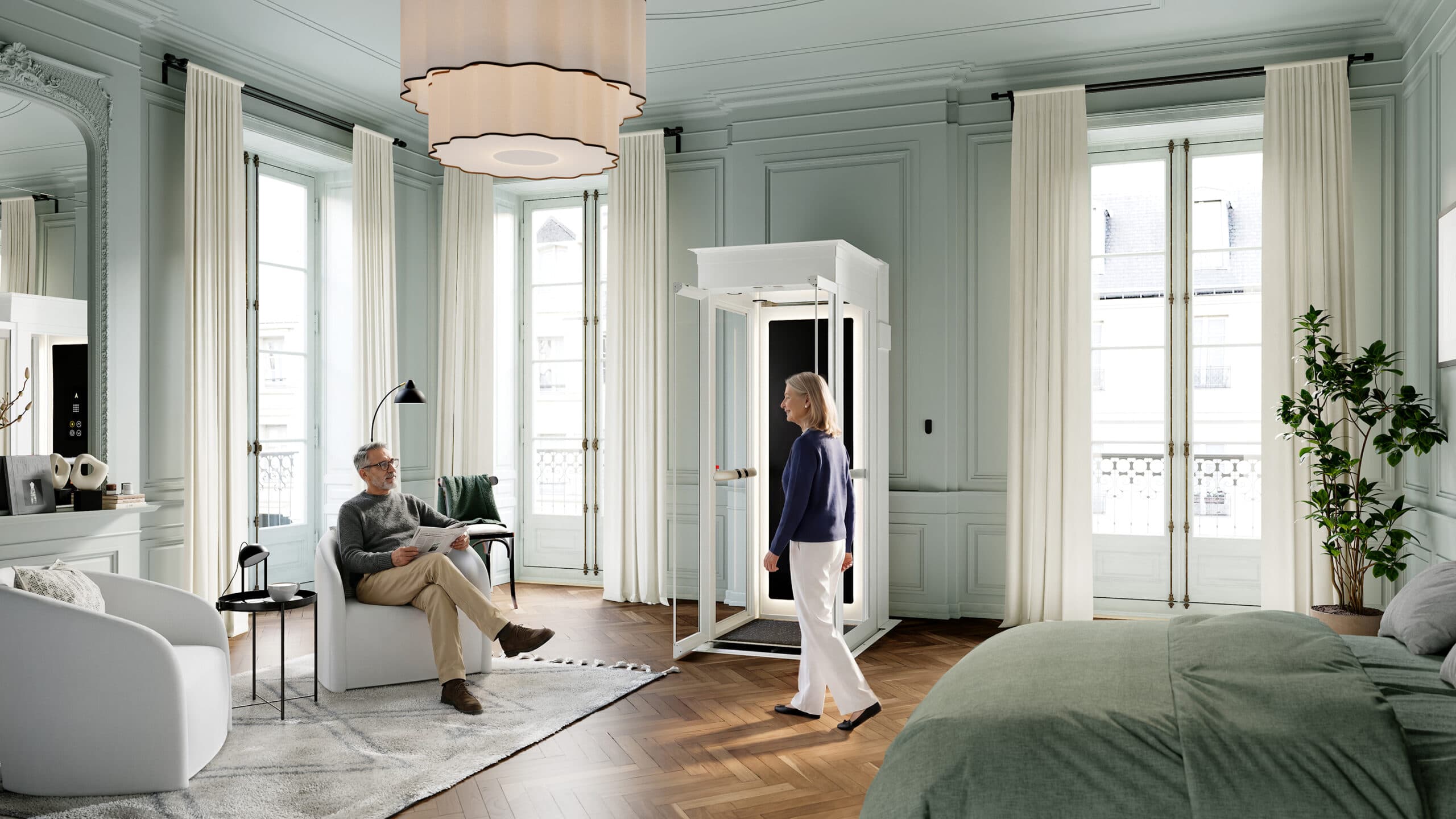 Appartement hausmannien avec de grandes fenêtres et de rideaux clairs, où l'on voit un homme assis dans un fauteuil blanc en train de lire le journal, une femme se dirigeant vers un petit ascenseur domestique Cibes Ascenda blanc, ainsi qu'un lit vert bien fait avec une plante en pot à proximité.